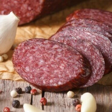 Sliced summer sausage on a board with garlic